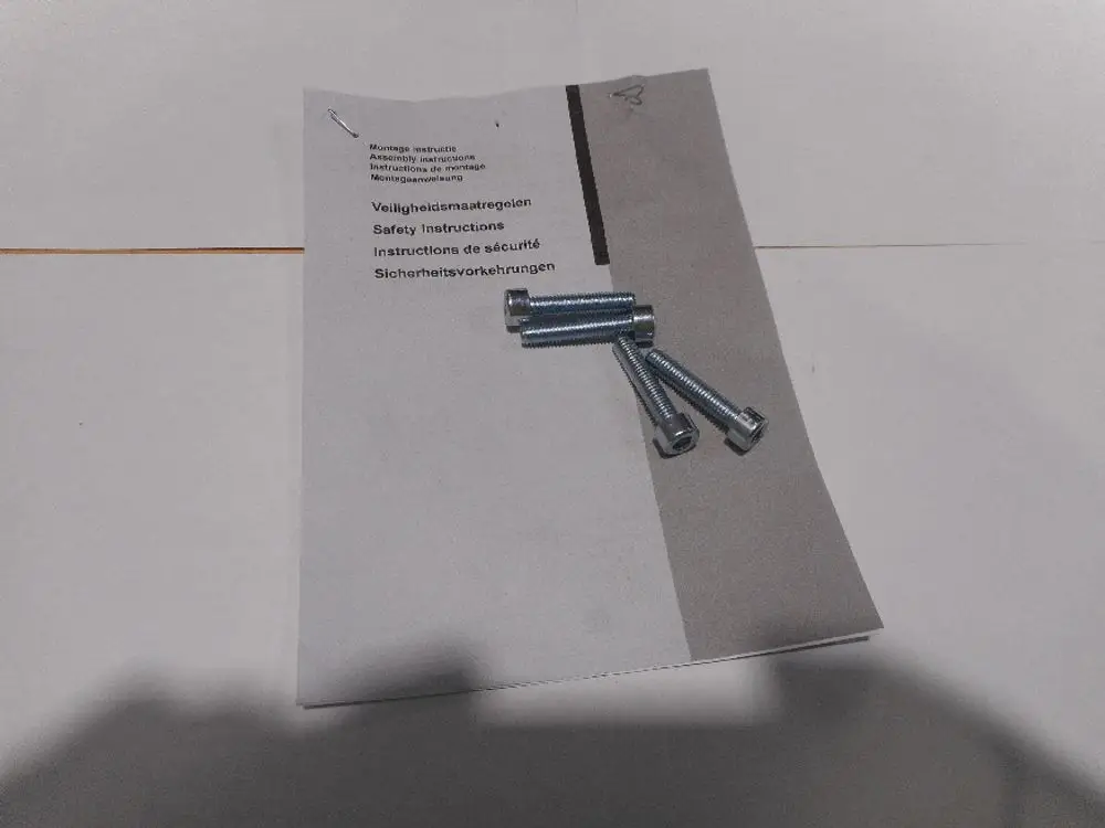 Blatt mit Montageanleitung von Remeha und mehreren Schrauben. Die Anleitung enthält Sicherheitshinweise in mehreren Sprachen, darunter Englisch und Deutsch.